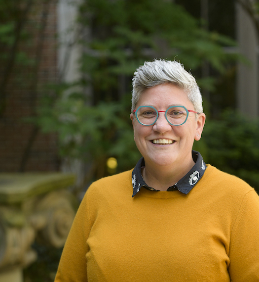 Headshot of Libby-a woman with short dark brown hair, glasses, wearing a yellow sweater and standing outside