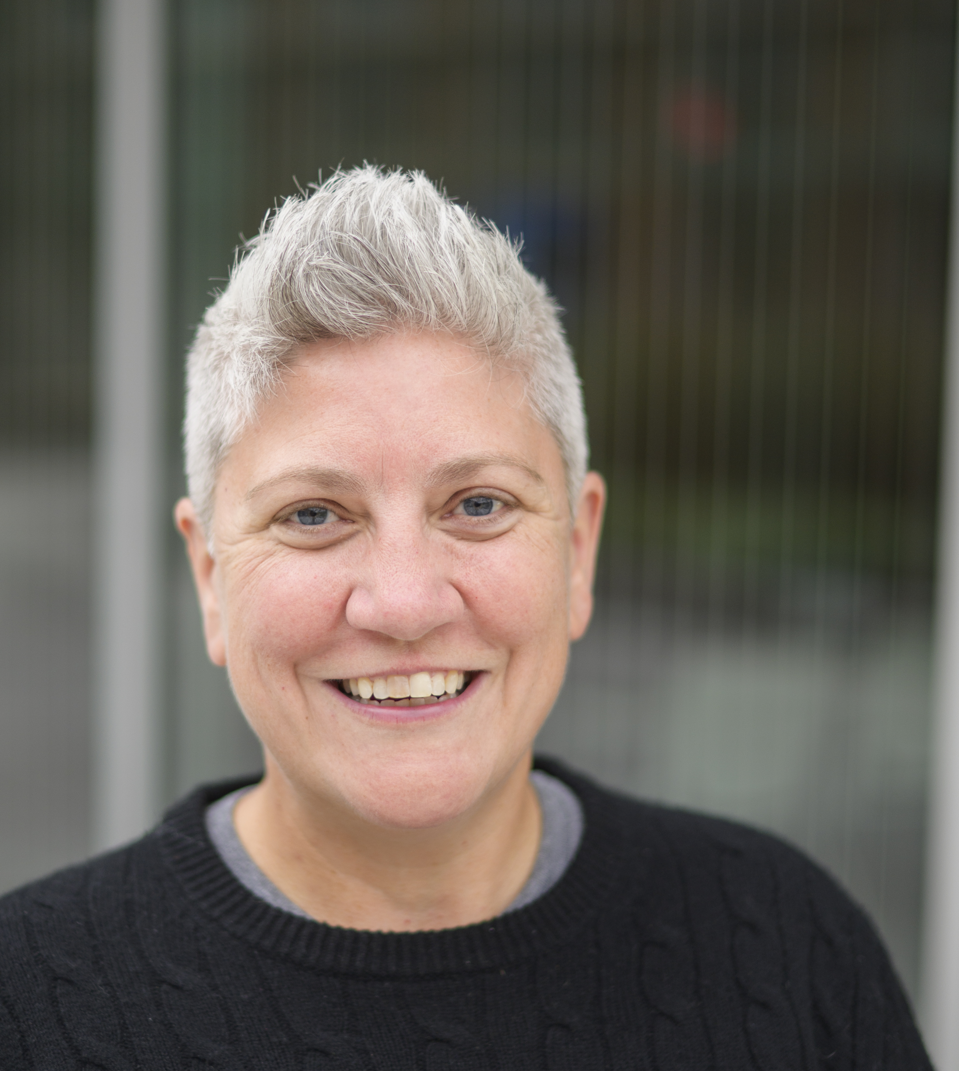 Headshot of Libby — a woman with short gray hair, smiling, and wearing a black sweater